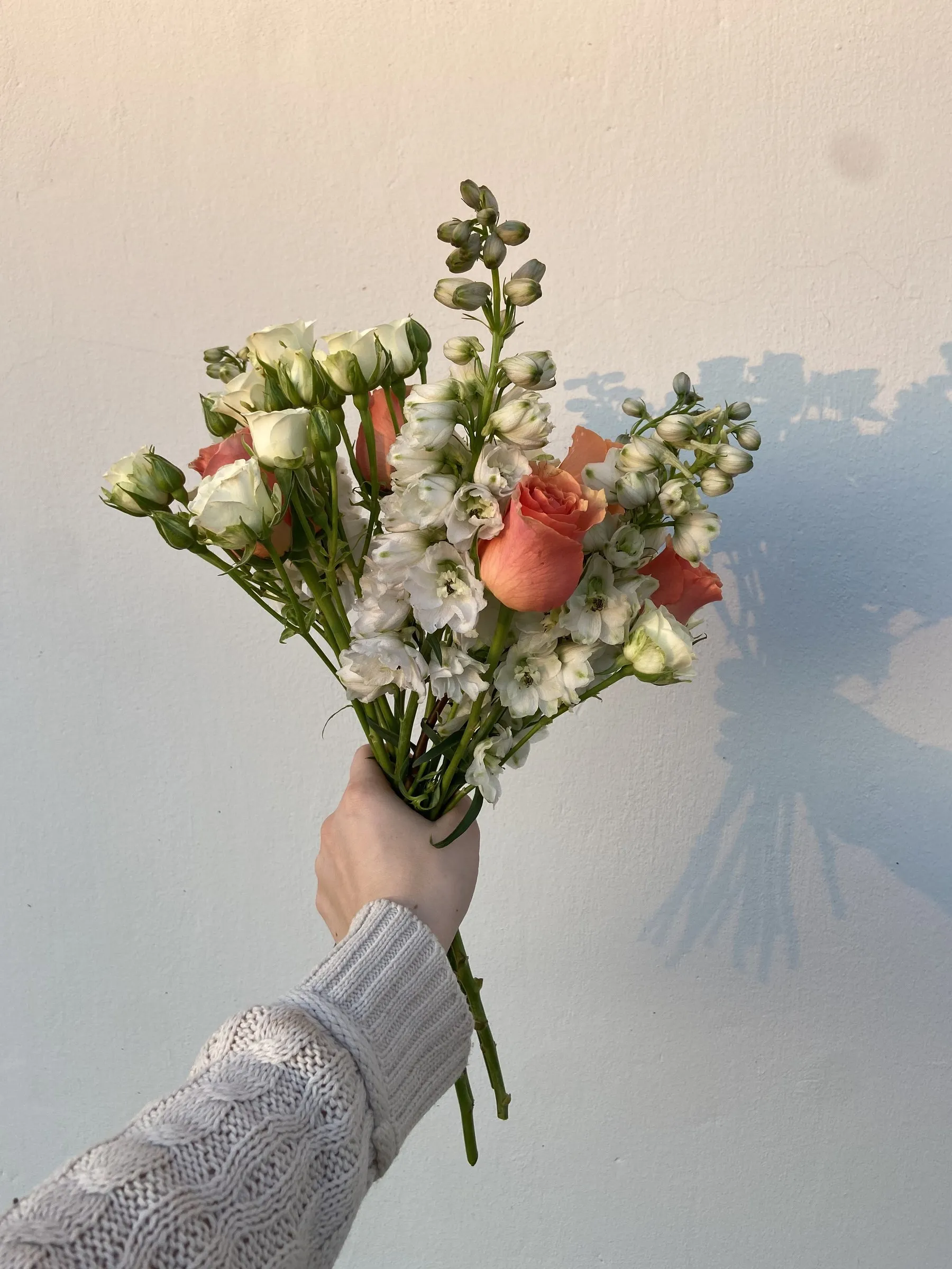 A peach and cream bouquet of snapdragons and roses held up against an open sky