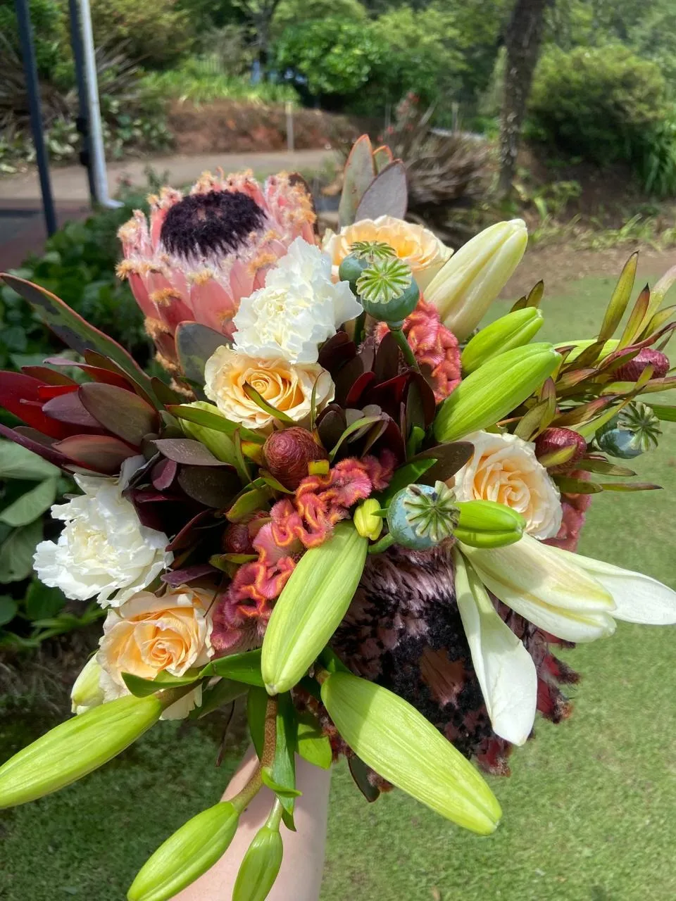 A bouquet of poppy seed pods, king protea, lilies and peach roses