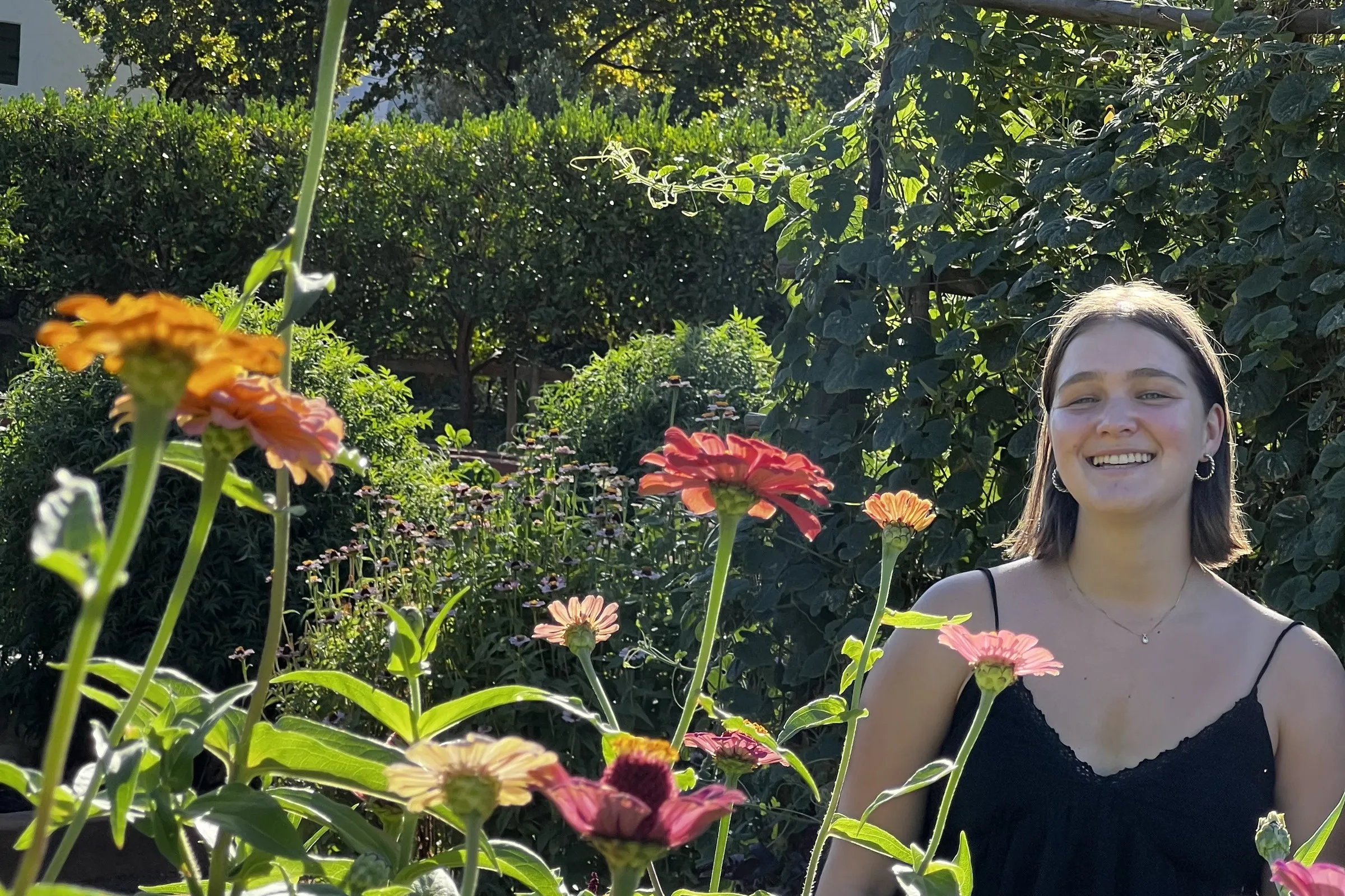A smiling florist standing among tall pink and orange zinnias in the cutting garden