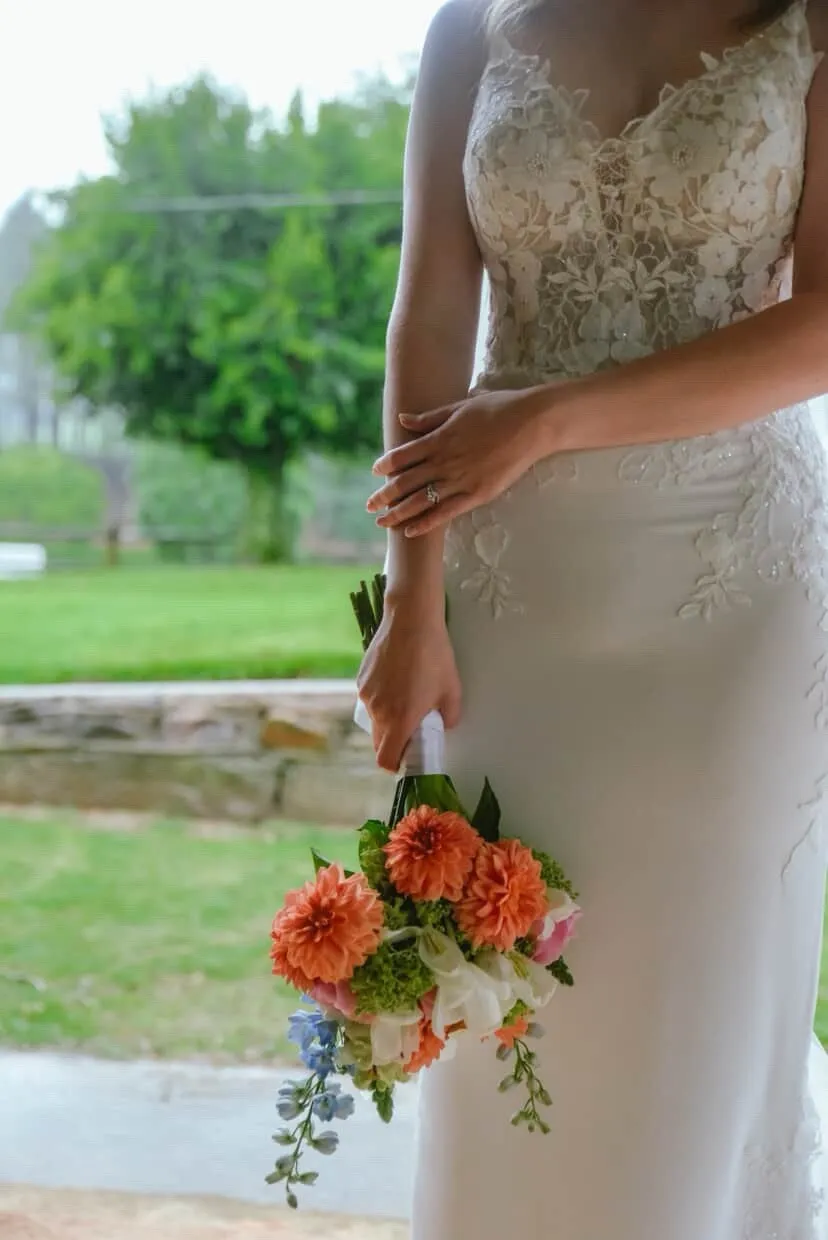 A bride walking outdoors carrying a bouquet of orange dahlias and pink blooms