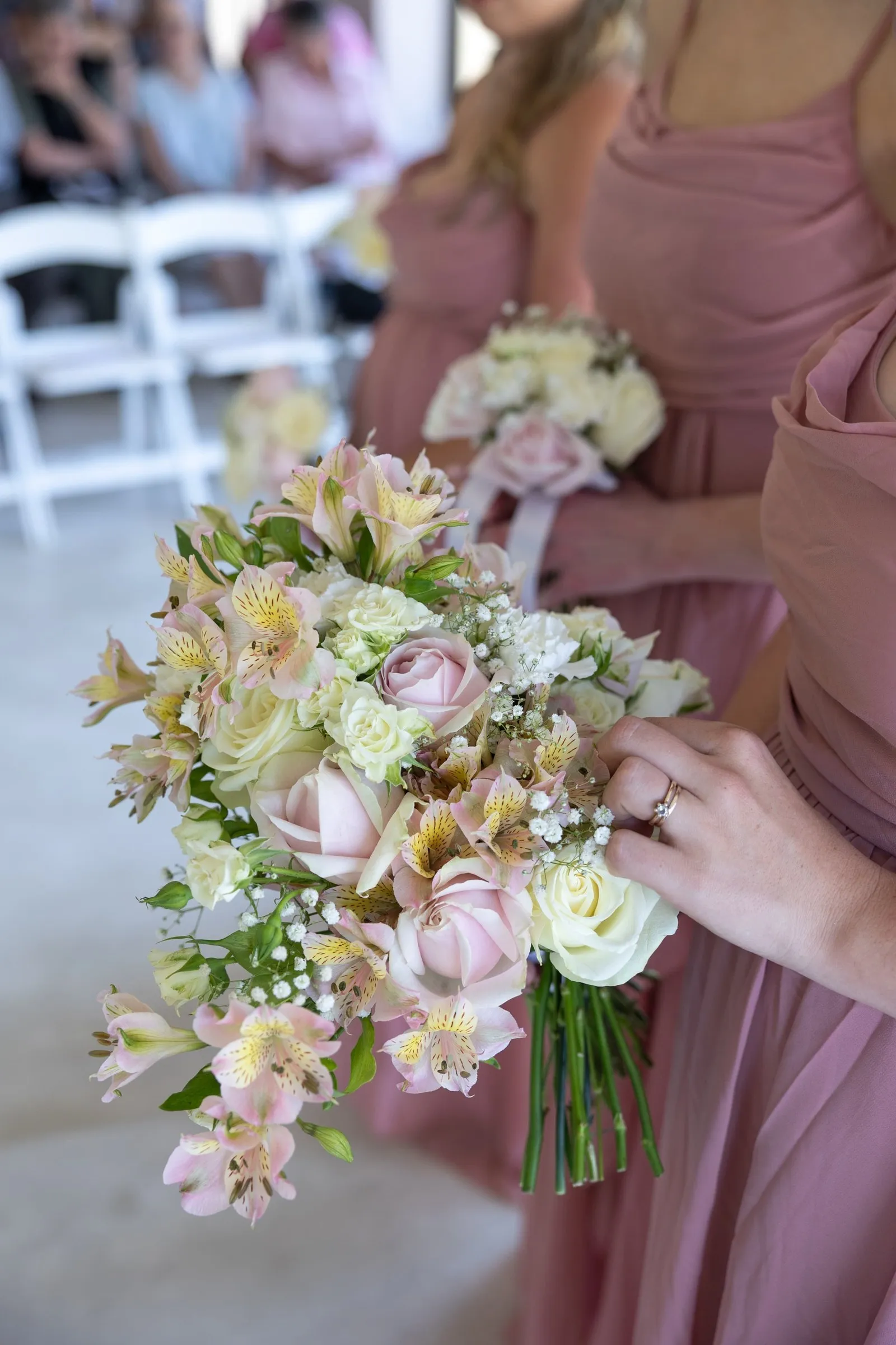 Bridesmaids holding soft pink and cream bouquets, an engagement ring in the foreground