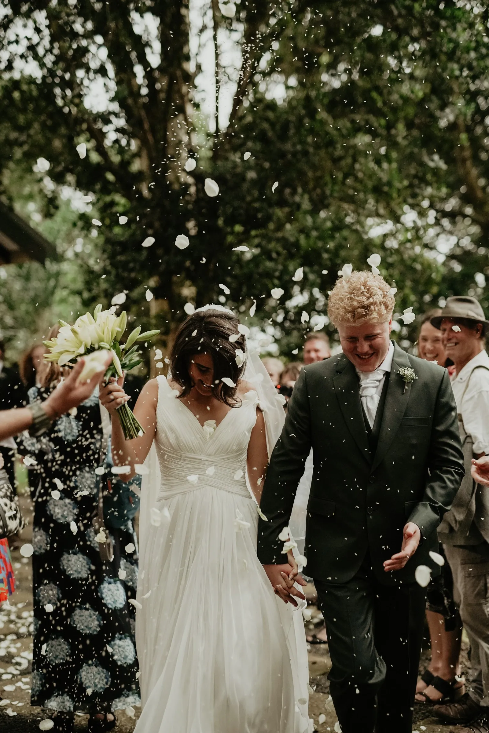 A couple walking out through a shower of confetti, the bride holding white blooms
