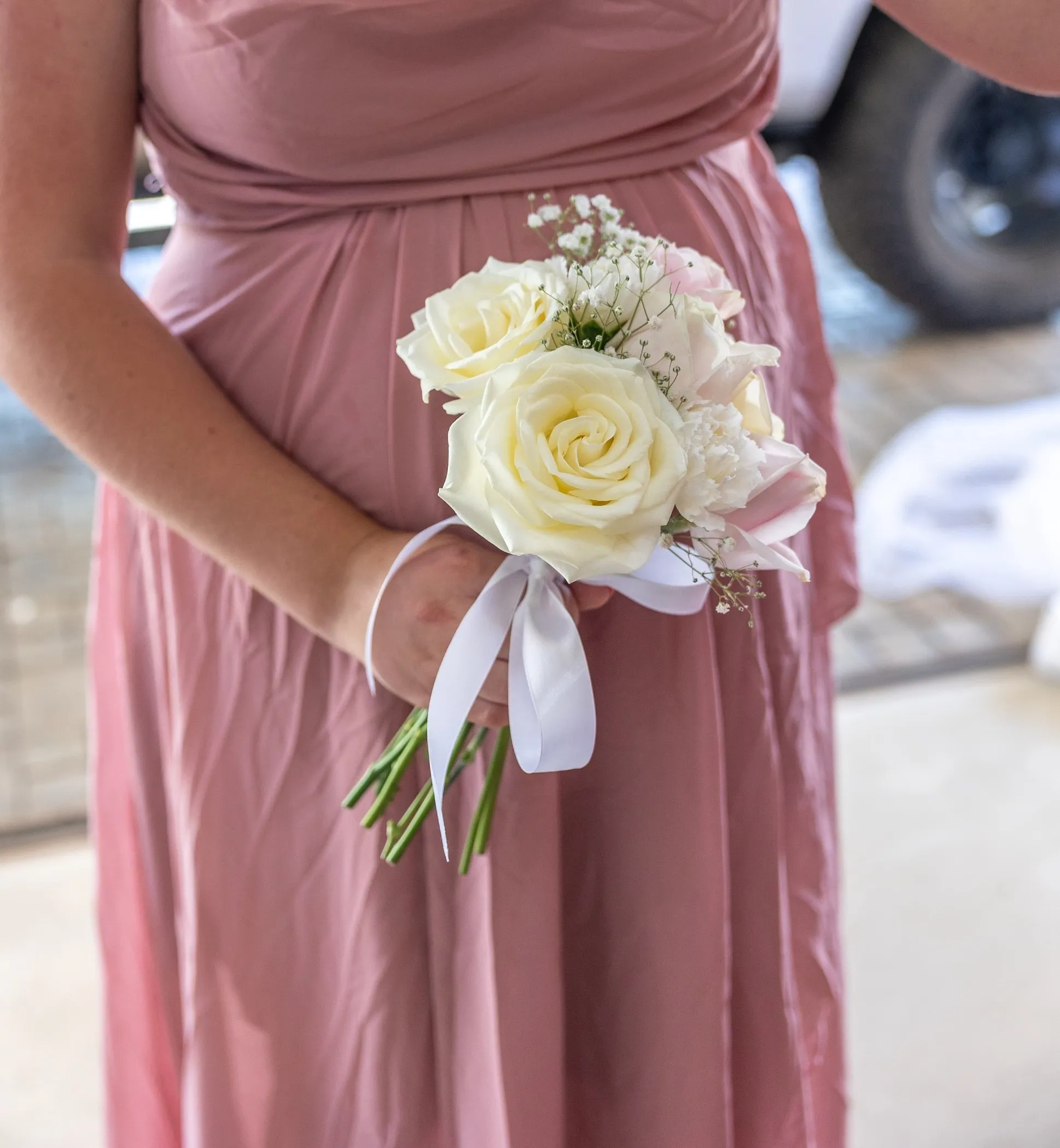 A small white rose corsage held against a dusty pink bridesmaid dress