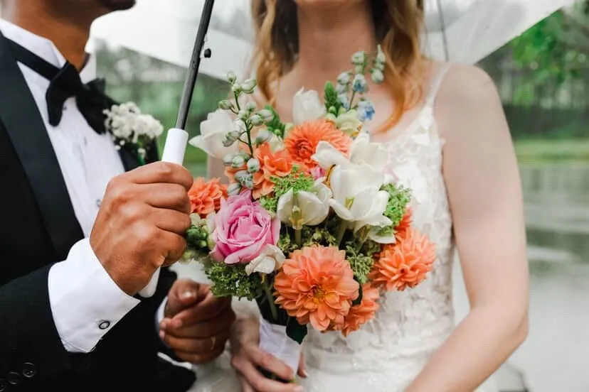A bright bouquet of orange dahlias, pink roses and white blooms held up by hand