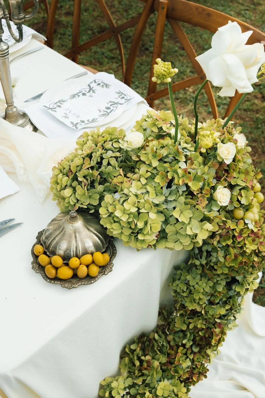 Green hydrangeas and white roses running along a reception table beside a silver urn